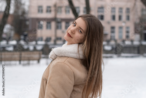 Portrait of long-haired brunette girl in beige sheepskin coat in winter outdoors. Young woman with light makeup on walk