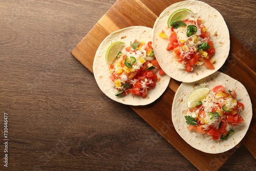 Delicious tacos with vegetables and lime on wooden table, top view. Space for text