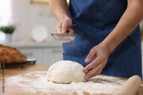 Making bread. Man sprinkling flour onto dough at wooden table in kitchen, closeup