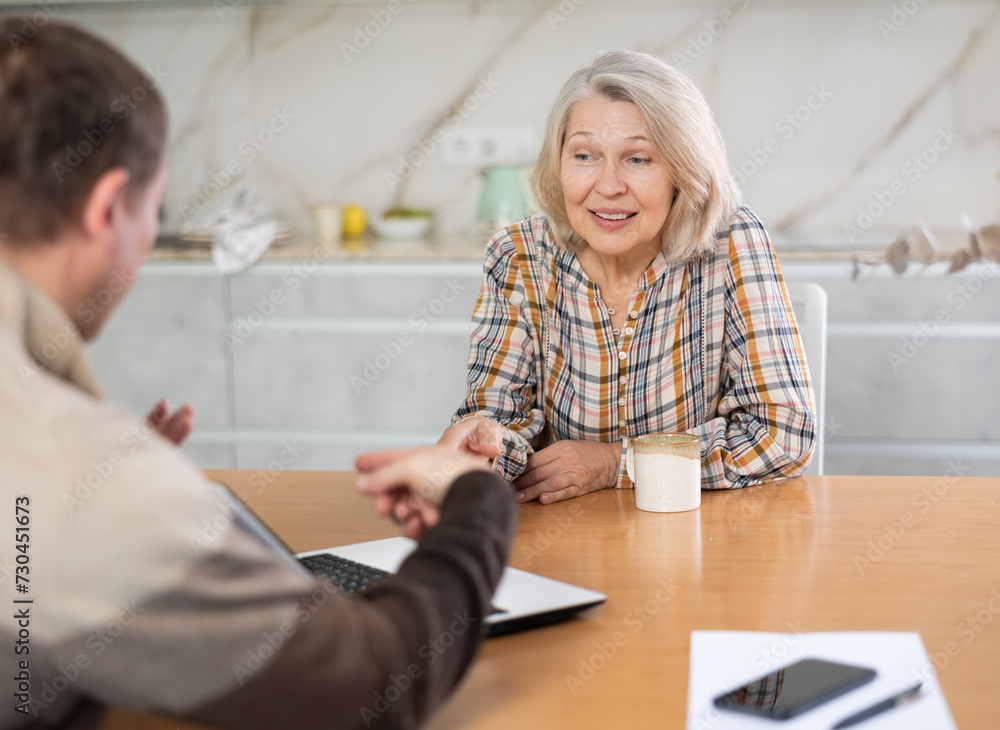 Fototapeta premium Male insurance agent tells an elderly woman the terms of an insurance contract. Offers to sign documents