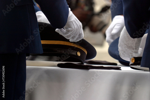 Horizontal close-up with detail of white gloves placing peaked military caps at the US Military table ceremony commemorating Memorial Day in the United States of America.