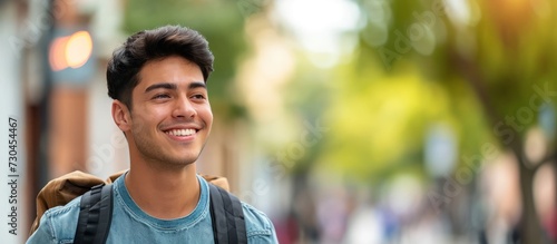 Confident young Hispanic man smiles while glancing sideways on a street.