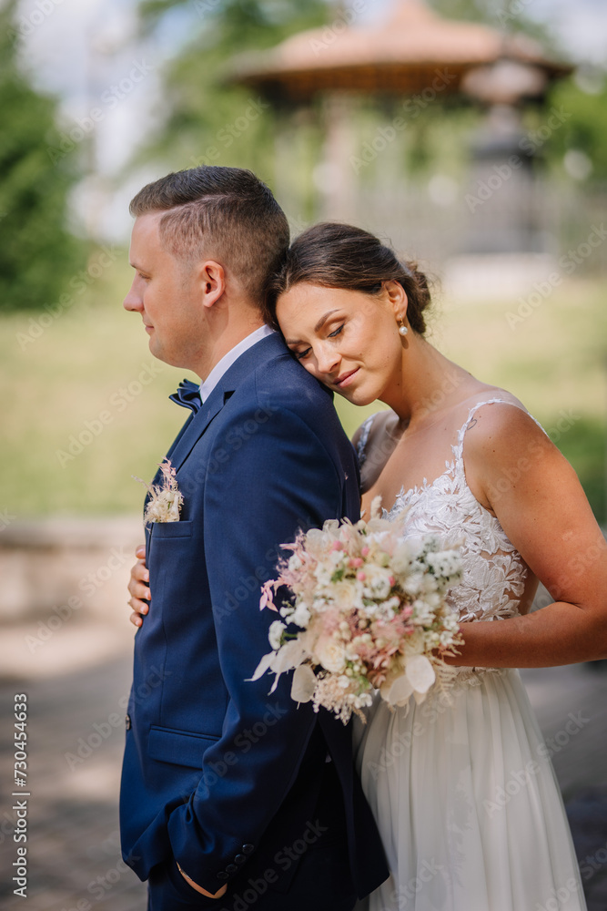 Valmiera, Latvia - July 7, 2023 - Bride leaning on groom's shoulder, both dressed in wedding attire, holding a bouquet, outdoors, gazebo in background, intimate, peaceful, affectionate. Valmiera, Latvia - July 7, 2023 - Bride leaning on groom's shoulder, both dressed in wedding attire, holding a bouquet, outdoors, gazebo in background, intimate, peaceful, affectionate.