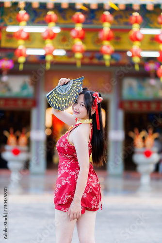 Portrait beautiful cute smiles Asian young woman wearing red traditional Chinese cheongsam decoration and holding a Chinese Fanning for Chinese New Year Festival at Chinese shrine in Thailand