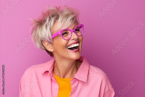 Portrait of a happy mature woman with pink hair and eyeglasses over pink background © Loli