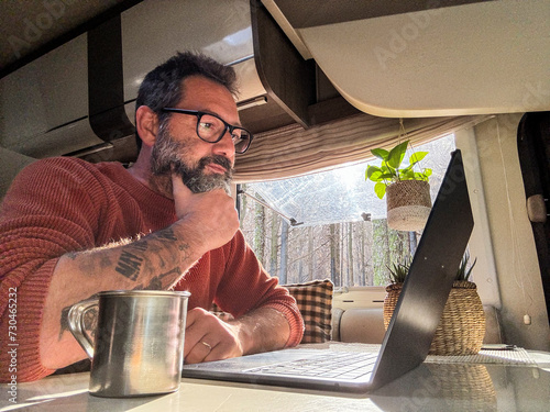 One digital nomad working inside a camper van travel lifestyle vehicle vanlife using laptop computer and roaming internet connection. People and telecommuting remote worker. Life in motorhome. Modern photo