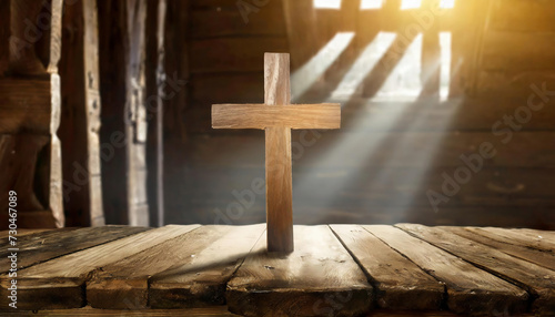 Wooden crucifix cross on wooden table in a medieval room on wooden table. Sun rays are seen spiritually from behind the cross. Copy space for your text