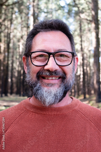 Cheerful adult happy man taking selfie picture in the woods enjoying outdoors leisure activity in national forestal park alone. Adventure and lifestyle people. High trees in background. Sustainability