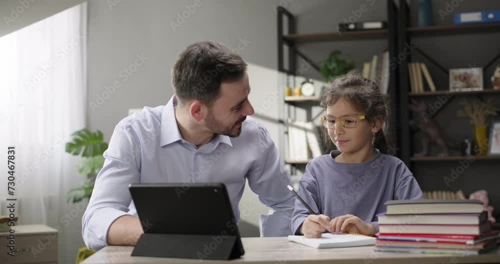 Father helping daughter doing homework at home desk. Father and daughter together studying online with digital tablet. Children remote education Father helping daughter doing homework at home desk. Father and daughter together studying online with digital tablet. Children remote education