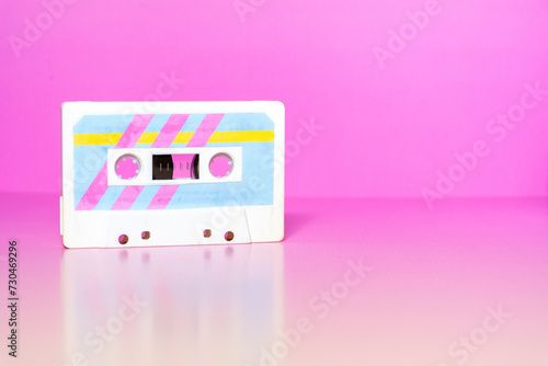 Audio cassette with colorful retro labels on a fuchsia background.