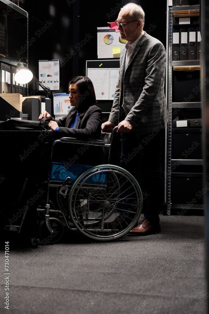 Obraz premium Paralyzed asian businesswoman executive sitting in wheelchair at office desk, inspecting quarterly results analysis data on laptop. Woman with paraplegia in accountancy workplace