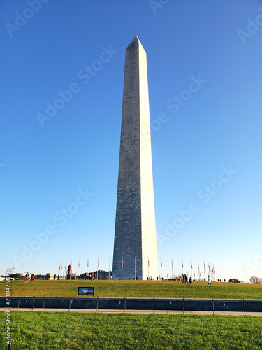 Washington Monument in Washington DC in clear blue sky day. People walk by the pond.