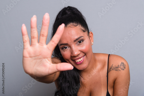 Beautiful happy brunette woman wearing black clothes making a sign with her right hand towards the camera.