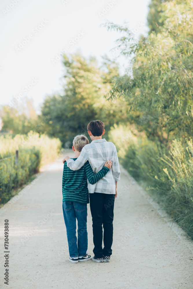 boys, brothers, little kids, wearing denim jeans and plaid hugging each other walking away from the camera down the wooded path pathway boys, brothers, little kids, wearing denim jeans and plaid hugging each other walking away from the camera down the wooded path pathway