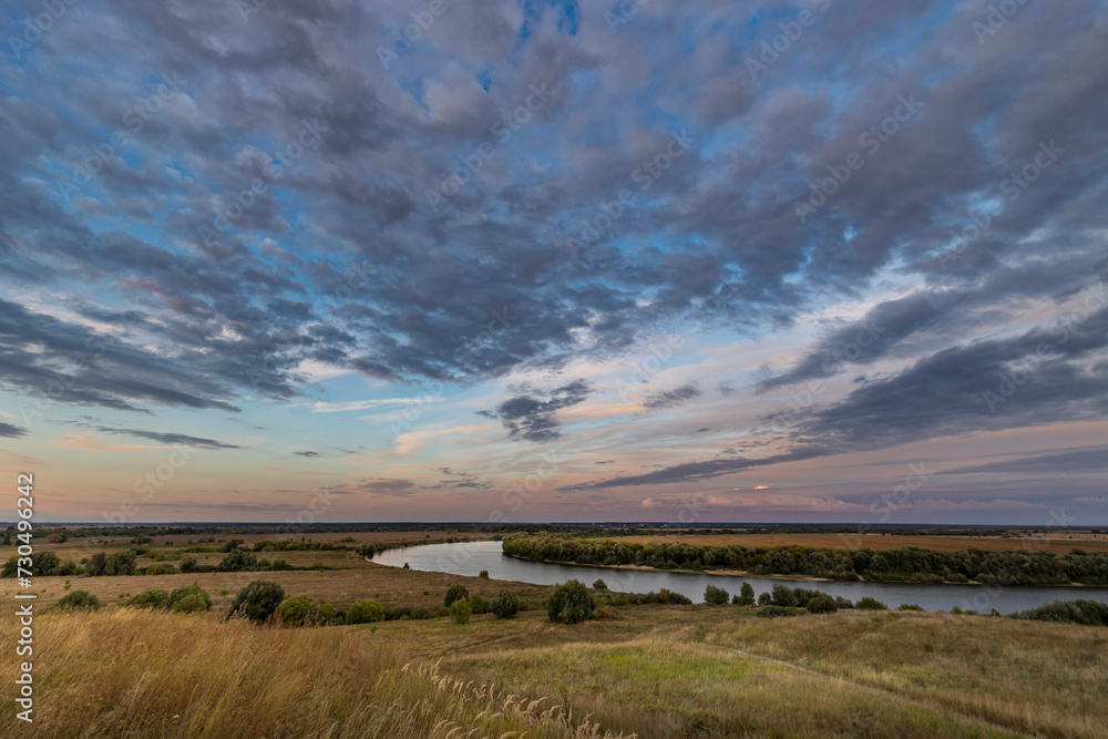 Evening landscape with dramatic sunset sky, endless fields, hills and a wide river bend