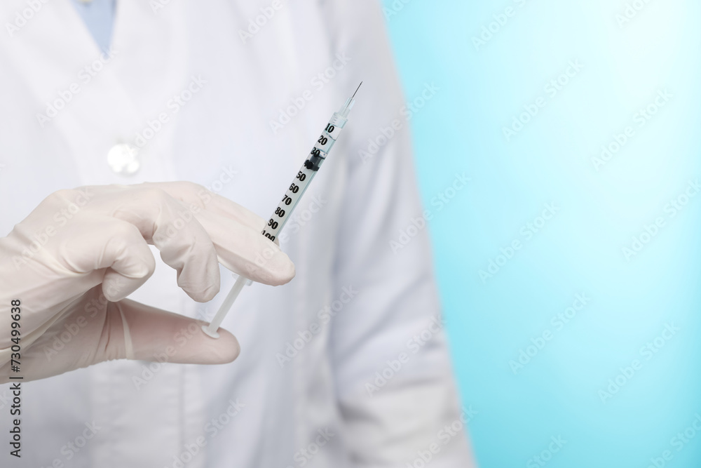 Doctor holding syringe on light blue background, closeup. Space for text Doctor holding syringe on light blue background, closeup. Space for text