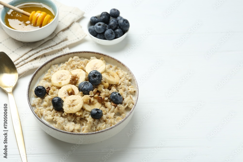 Tasty oatmeal with banana, blueberries, walnuts and honey served in bowl on white wooden table, space for text Tasty oatmeal with banana, blueberries, walnuts and honey served in bowl on white wooden table, space for text