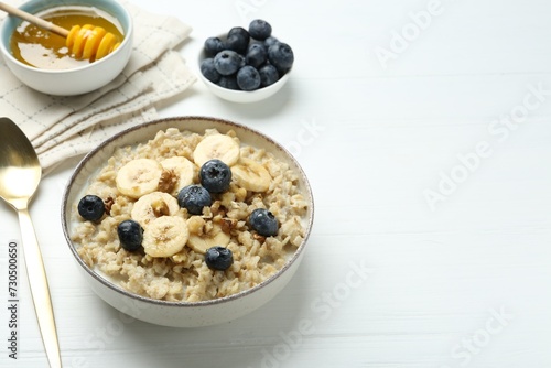 Tasty oatmeal with banana, blueberries, walnuts and honey served in bowl on white wooden table, space for text