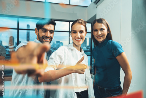 Happy businesspeople pointing at glass wall while standing with confident. Group of businesspeople looking at camera while standing at transparent board with business idea, strategy, planing. Tracery.