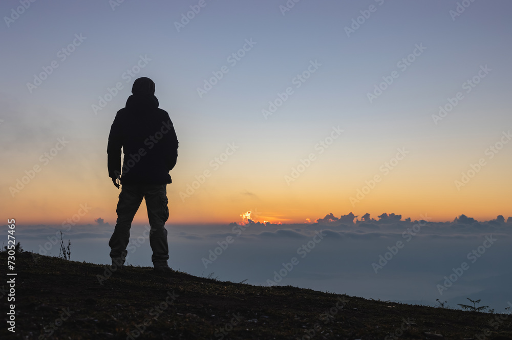 Young man standing alone on top mist mountain and staring at sunrise, cloudy sky. Young man standing alone on top mist mountain and staring at sunrise, cloudy sky.