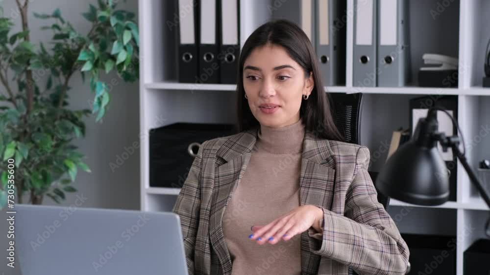 Smiling Caucasian woman employee talking in video call using laptop in her spare time in office. Greeting, waving hand, active and joyful conversation. Smiling Caucasian woman employee talking in video call using laptop in her spare time in office. Greeting, waving hand, active and joyful conversation.