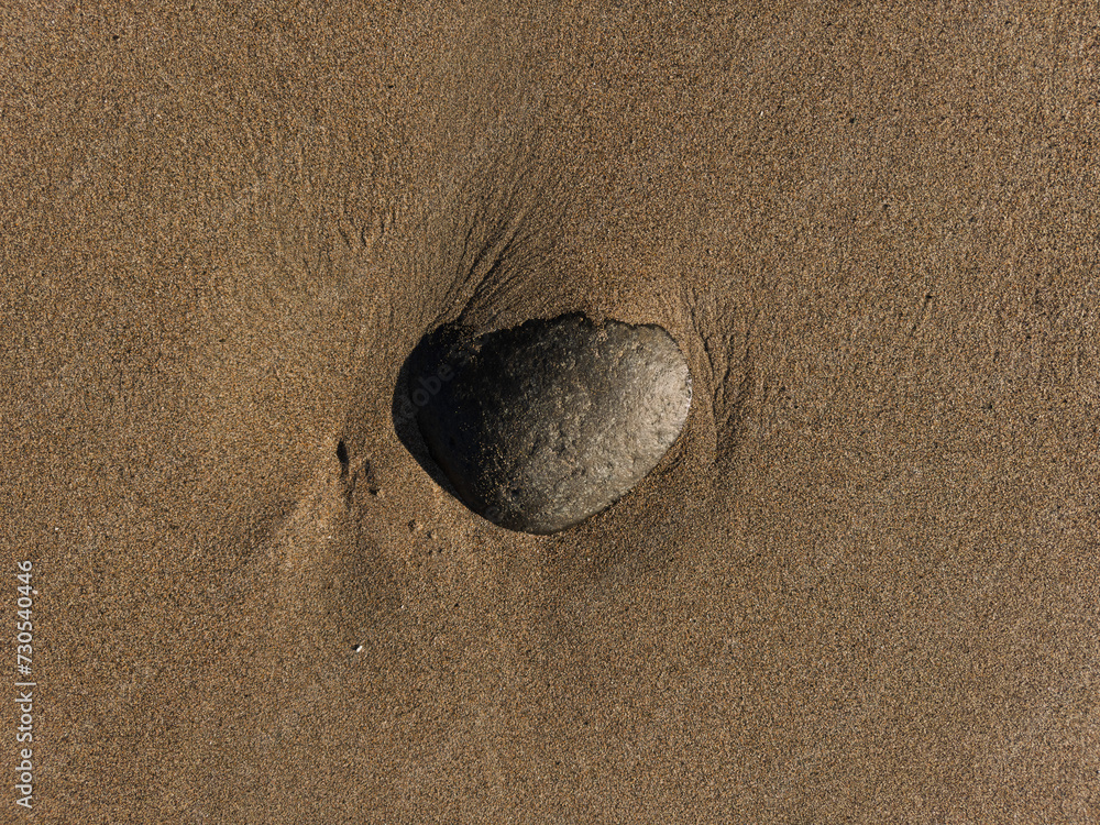 A smooth, weathered stone buried in the sand on a beach in San Francisco. A smooth, weathered stone buried in the sand on a beach in San Francisco.