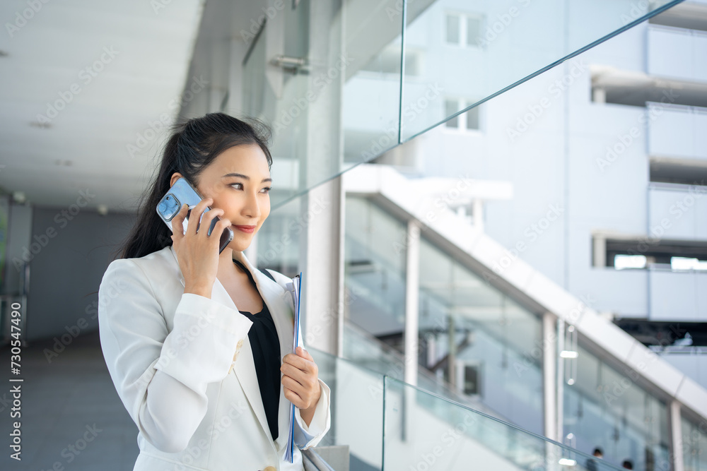 Young businesswoman holding document and using a smartphone while walking through the city Young businesswoman holding document and using a smartphone while walking through the city