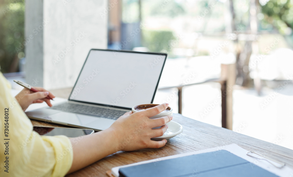 Close-up shot, young asian woman in casual clothes holding coffee cup while working with laptop at outdoor cafe Close-up shot, young asian woman in casual clothes holding coffee cup while working with laptop at outdoor cafe
