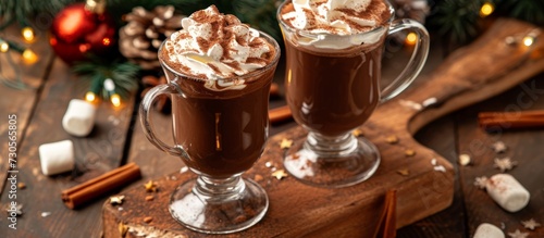 Hot chocolate with whipped cream, marsmallow, and cocoa powder is a winter and autumn Christmas drink served in two glasses.