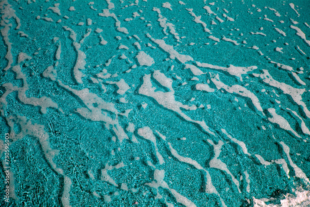 Abstract view with sea waves texture. Foam of sea waves in color abstraction. The structure of the sea surf in shallow water is specially tinted in different colors. View from above.