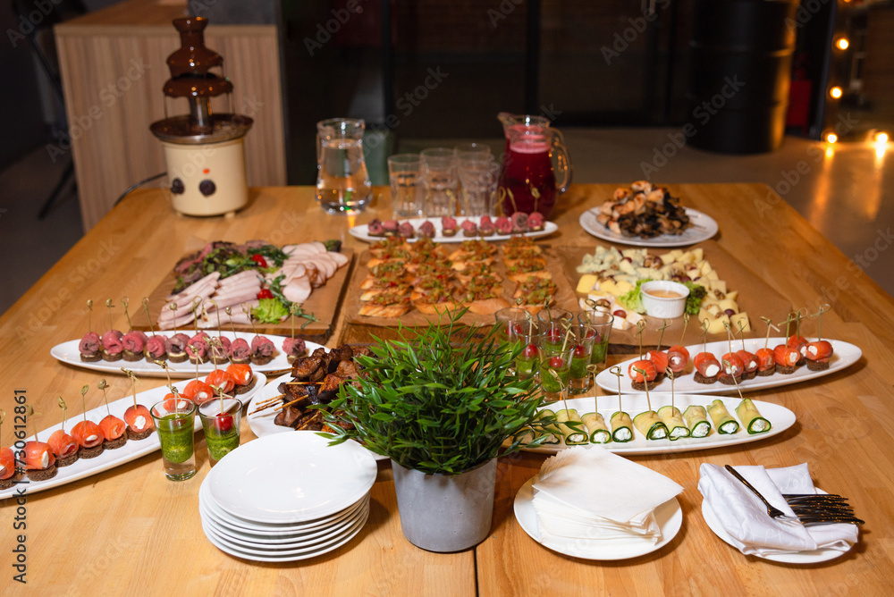 Catered Buffet Table with Assorted Gourmet Dishes. An elegantly arranged buffet table featuring a variety of gourmet dishes including canapés, skewers, and a chocolate fountain, ready for an event.