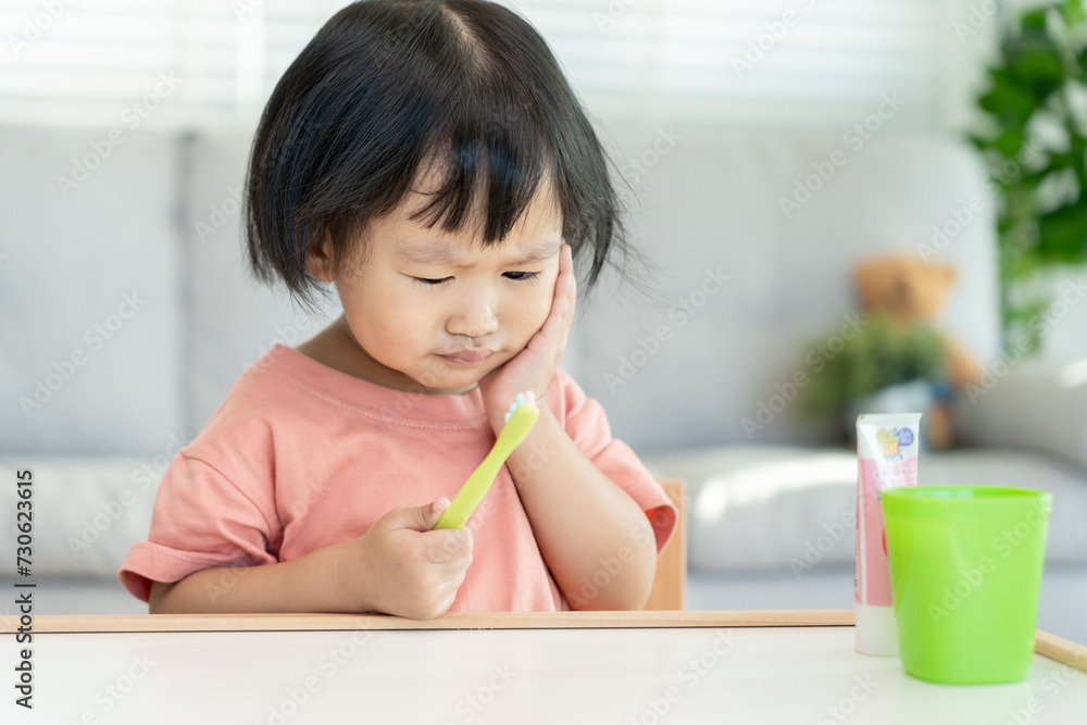 little asian girl presses hand to cheek, suffers from pain in tooth. Teeth decay, dental problems, child emotions and facial expression, oral health care, reducing sweets, fluorine coating little asian girl presses hand to cheek, suffers from pain in tooth. Teeth decay, dental problems, child emotions and facial expression, oral health care, reducing sweets, fluorine coating