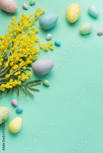 Festive Easter Decoration With Colorful Eggs and Mimosa Flowers on a Pastel Green Background