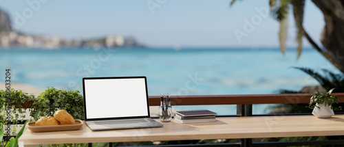 A remote workplace with a laptop mockup on a table on a balcony with a beautiful ocean sea view.