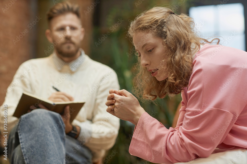 Fototapeta premium Side view portrait of struggling young woman sharing mental health problems with psychologist in therapy session, copy space