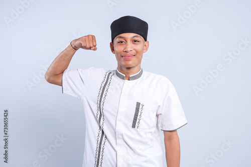Young Asian muslim man wearing cap showing strong hand isolated over white background