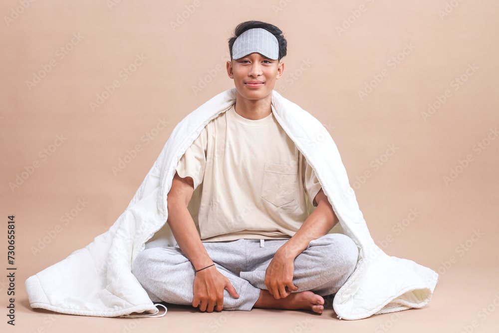 Man with sleep mask sitting cross-legged on the floor, covered with blanket and looking at camera Man with sleep mask sitting cross-legged on the floor, covered with blanket and looking at camera