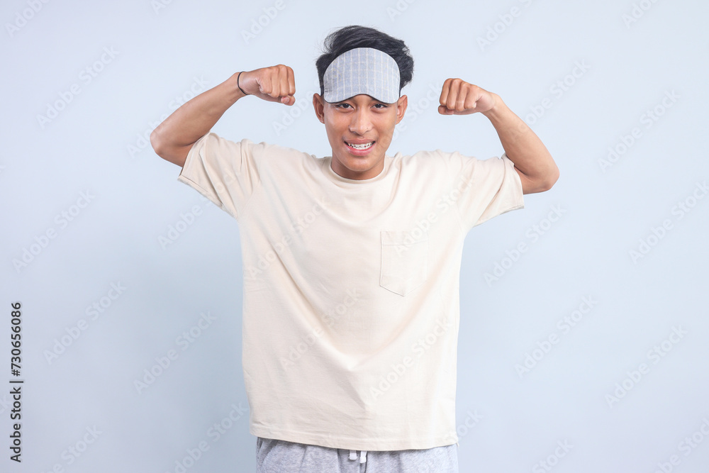 Excited young guy wear eye mask showing strong hands bicep muscle isolated over light blue background Excited young guy wear eye mask showing strong hands bicep muscle isolated over light blue background