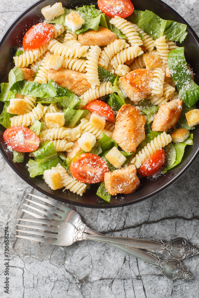Caesar salad fusilli pasta with chicken, romaine lettuce, parmesan, tomatoes and croutons close-up in a bowl on the table. Vertical top view from above Caesar salad fusilli pasta with chicken, romaine lettuce, parmesan, tomatoes and croutons close-up in a bowl on the table. Vertical top view from above