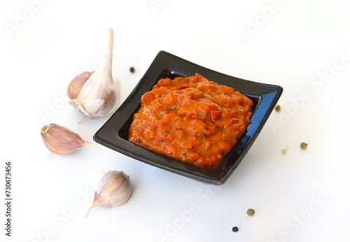 Bowl of red sauce, close-up,garlic on a white background. Homemade sauce, seasoning,spicy paste. Bulgarian lutenitsa, aur Balkan ajvar, with tomatoes, eggplants, paprika, garlic. Traditional seasoning