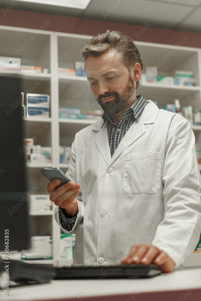 Male pharmacist using the computer and phone while working at the pharmacy Male pharmacist using the computer and phone while working at the pharmacy