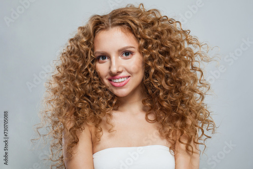 Joyful redhead female model with long frizzy ginger hair and clean soft fresh skin posing on white background. Studio fashion beauty portrait of young woman