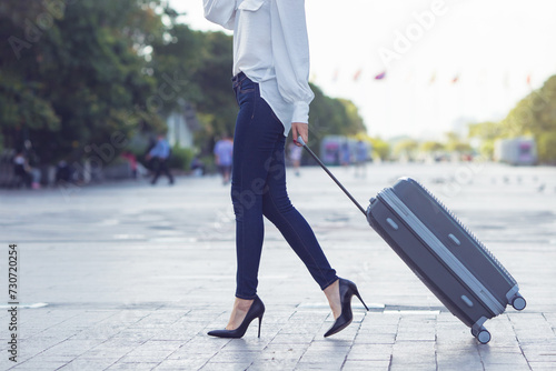 Young female traveler walking with a gray suitcase at the modern transport stop outdoors, travel concept of vacation and holiday.