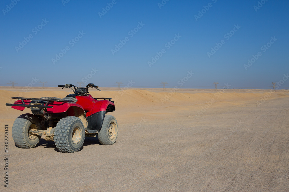 Red quad bike in the Arabian desert standing on safari road. Concept of active extreme sports in the sandy desert on sunny day Red quad bike in the Arabian desert standing on safari road. Concept of active extreme sports in the sandy desert on sunny day