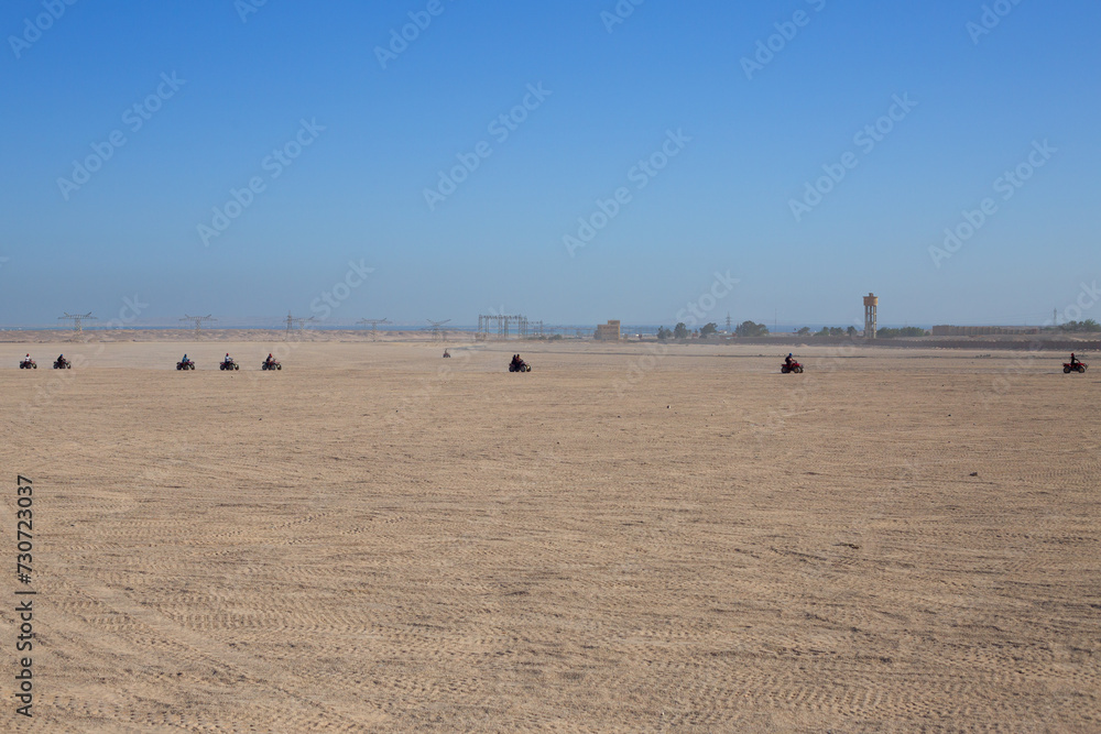 Extreme excursion on ATV in desert with a group of tourists riding one after another on the sand against the backdrop of a clear sky