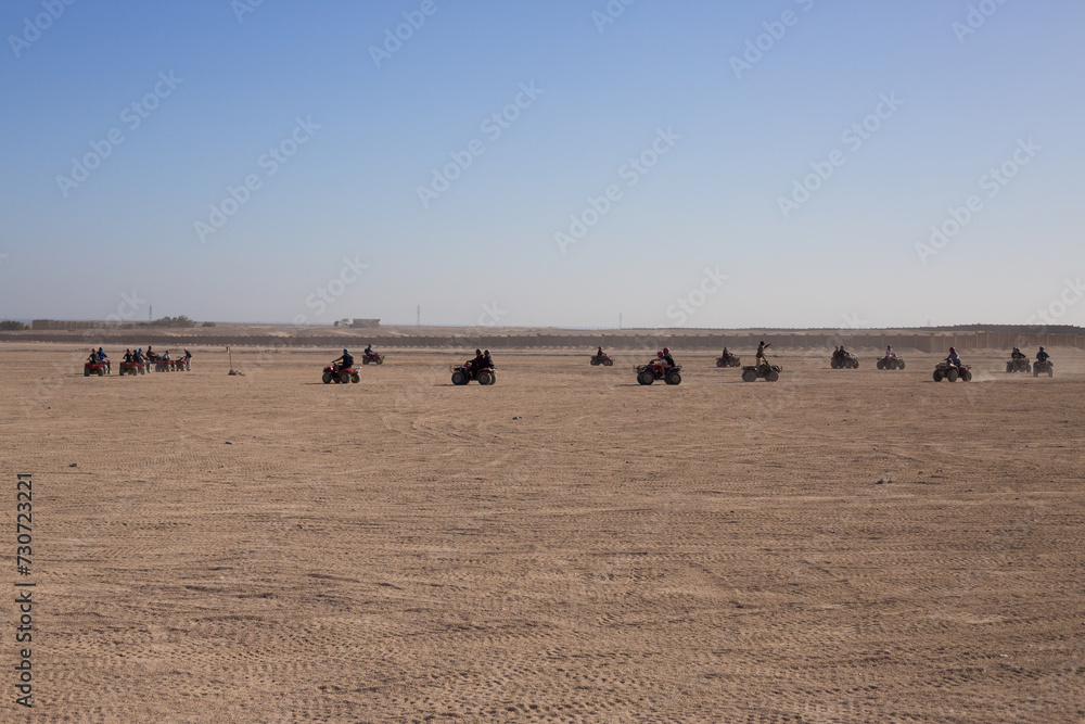 Obraz premium Group of tourists on ATVs during an excursion through the Arabian desert in Egypt. Extreme holiday in the desert on hot day