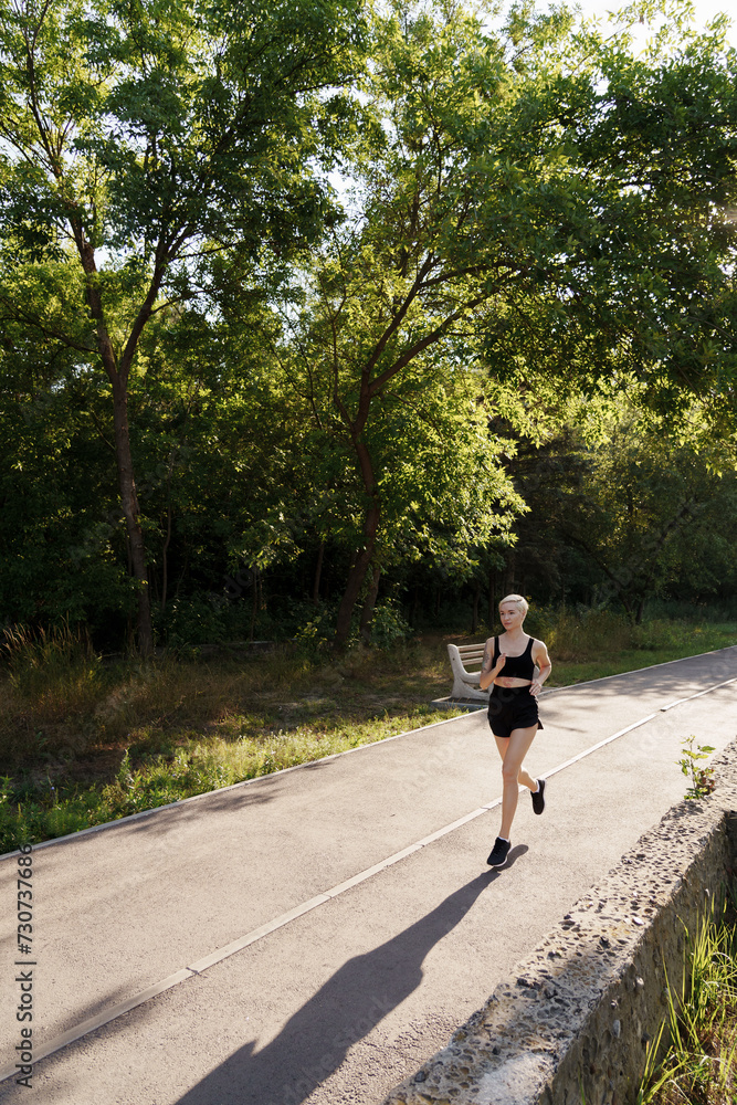 A woman jogs on a serene park path, casting a long shadow