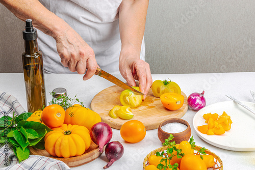 A woman is preparing a tomato salad. Ripe vegetables, herbs, aromatic spices, olive oil