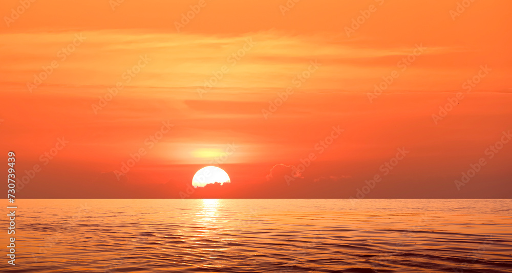 Colorful dramatic sunrise sky background over sea with the sun going up behind cloud and golden sunlight reflection on water surface in the morning. Beautiful Idyllic summer seascape view