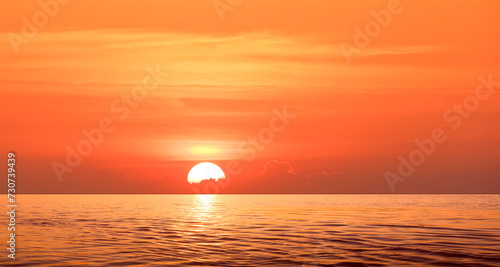 Colorful dramatic sunrise sky background over sea with the sun going up behind cloud and golden sunlight reflection on water surface in the morning. Beautiful Idyllic summer seascape view